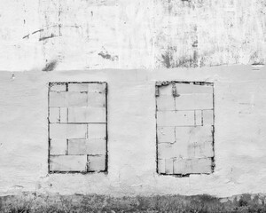 Old abandoned crumbling plaster  facade building wall  with walled windows black and white