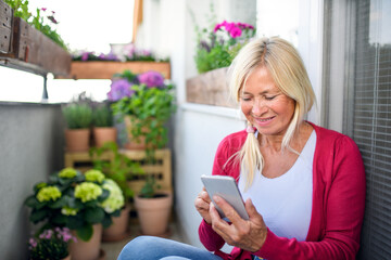 Senior woman relaxing on balcony in summer, using smartphone. - Powered by Adobe