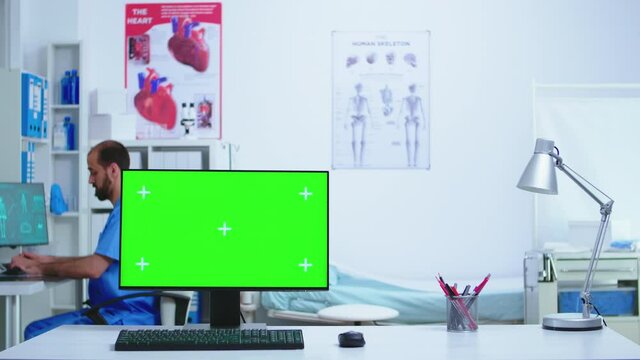 Doctor and her assistant checking patient x-ray and computer with green display in hospital. Desktop with replaceable screen in medical clinic while doctor is checking patient radiography for diagnose