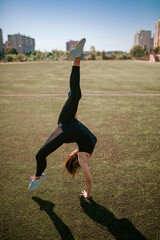 young good looking girl in black sport outfit doing gymnastics handstand in the splits in park with ball