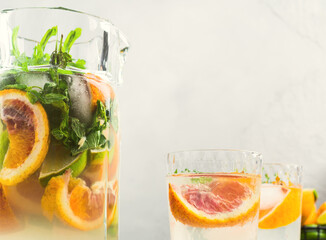 Fresh summer citrus lemonade cocktail with lime, mint and blood oranges in large glass jar and...