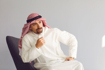 Pensive arab businessman sitting in a chair thinks looks up on a gray background. Portrait of an attractive arab man.