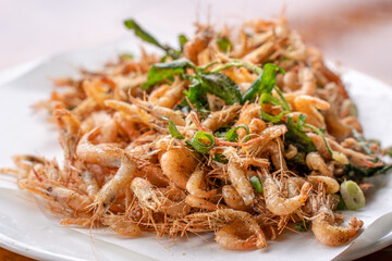 Salted fried crispy river shrimp prawn, Macrobrachium nipponense, in a white plate on wooden table, delicious Taiwanese street food, lifestyle.