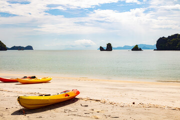 Two yellow kayak boats lie on the sandy beach of Tanjung Rhu Beach in Langkawi, Malaysia. Idyllic view over the beach. White clouds on blue sky. In the background the rocks in the water off the coast
