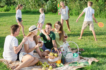 Four adult people on picnic outdoors on background with children playing active games.