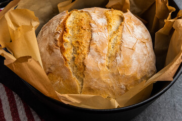 Rustic white bread baked in a cast iron dutch oven, just out of the oven, placed on a slate countertop with a kitchen towel waiting to cool before removing