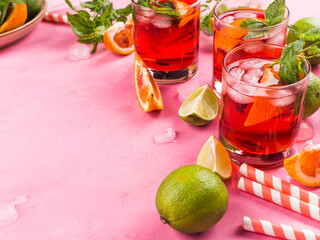 Pink background with ingredients for summer iced red cocktail with blood orange and lime