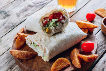 Doner kebab or shawarma. Grilled chicken in pita bread with tomatoes, corn and green salad on wooden board. Rustic wooden background. Middle Eastern food, arabic fast food concept