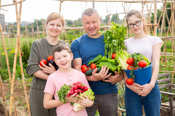 Portrait of positive family of four in backyard garden with gathered greens and vegetables