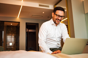 Portrait of a men laughing while looking at laptop in the hotel room.