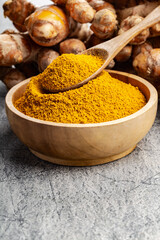 Turmeric powder in wooden bowl on grey concrete background.