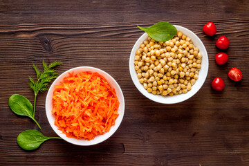 Vegetarian meal. Chickpeas and carrot in bowls on dark wooden table top view