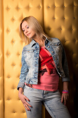 Portrait of a girl blondes in a denim suit on a background of a golden wall.
