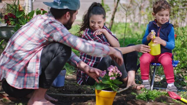 Fun time mam and dad playing with their small charismatic son with sprinklers while sitting on the chair in the middle of garden they have a good time