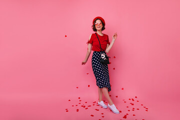 Full-length portrait of caucasian woman in stylish dress standing under confetti. Magnificent french girl celebrating valentine's day.