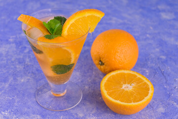 
A glass of refreshing orange cocktail with mint and ice on a blue bright background.