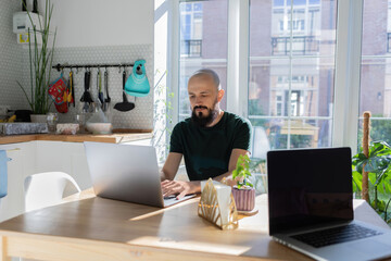 The guy works from home. He sits in the kitchen at the table and uses a laptop computer and drink hot tea. His business is going well.