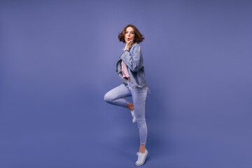 Full-length portrait of amazed beautiful lady in jeans. Curly curious girl jumping on violet background.
