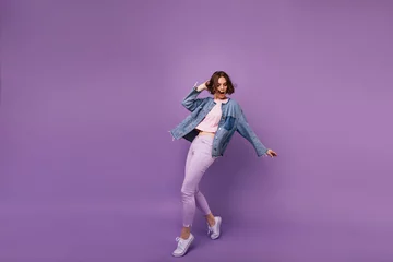 Fotobehang Full-length portrait of attractive slim girl wears white sport shoes. Indoor photo of enchanting caucasian woman dancing on violet background. © Look!