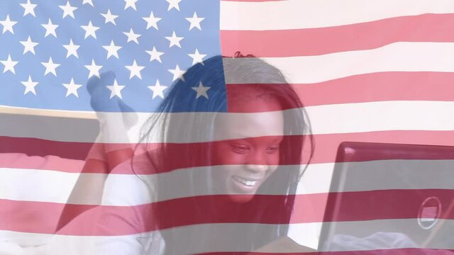 Animation of American flag waving over happy African American woman lying on bed