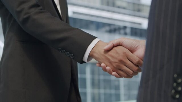 Close up. Hand of two Asian business people gathered to shaking hands agree to a deal or say hello On the background of building in city