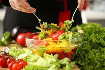 Close up of male hands mixing greenery and vegetables in bowl with spoon for dinner