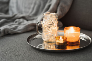 Decorative lights in a glass jar and burning aroma candles on a metal tray. Home decor for cozy atmosphere