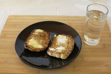 Two slices of toast and a glass of water with spread that is melting.

