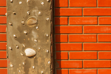 A bright red brick fence with a gray concrete pillar with seashells.