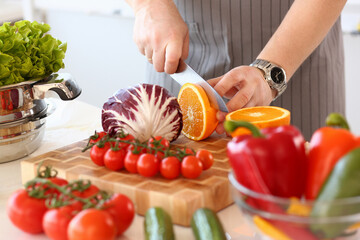 Close up of male hands using board and knife for cooking fruit and vegetable salad at home