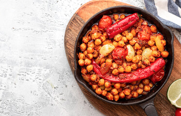 Spicy chickpeas with hot red peppers, tomatoes, cumin, garlic and other spices in a frying pan on a grey background top view. Chickpeas stewed with vegetables and spices. Free space for text