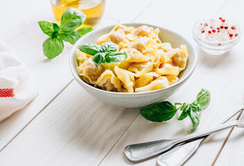 Tortellini with cheese sauce, basil leaves in bowl on white wooden background.