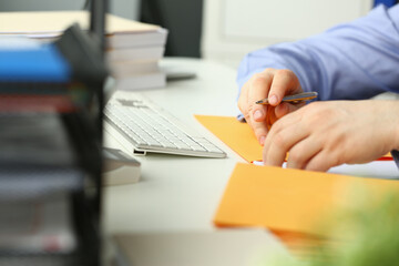 Close up cropped head of male hands as he is sitting at workplace in office and using pen for...