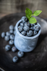 shadow falls on fresh blueberries in small blue ceramic jar with green leaf on top