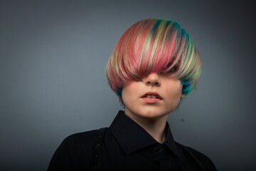 Nice portrait of young white girl in black shirt with rainbow color hair on grey background