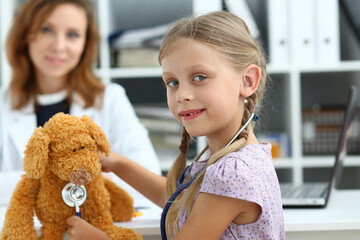 Profile portrait of smiling kid using stethoscope for toy while visiting female pediatrician in hospital