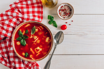 Tomato soup with tortellini in white bowl on white wooden table.