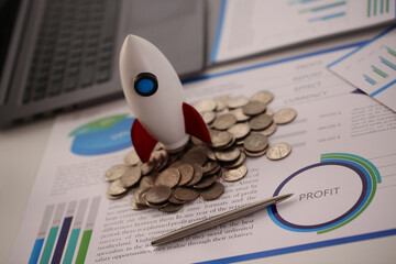 Top view close up of plastic little missile standing on money and some financial charts on desk in office near laptop