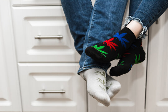Lovers sit in the kitchen and touch their feet. A guy with a girl. The legs are wearing jeans and socks with the image of marijuana. Added noise. Close-up.