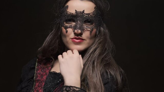 Halloween. Beautiful queen in cloak with crown at dark background. Portrait of young brunette vampiress. Close-up in 4K, UHD