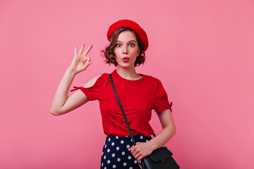 Surprised stunning girl in red t-shirt funny posing in studio. Indoor shot of spectacular female model in beret expressing surprised emotions.