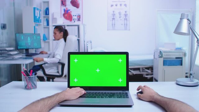 Pov shot of physician using laptop with chroma key in hospital cabinet and doctor looking at x-ray image. Medic using notebook with green screen on display in medical clinic.