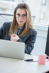 manager bionda vestita in giacca scura e occhiali da vista  è seduta nella sua postazione di lavoro mentre  indica qualcosa nel computer 
