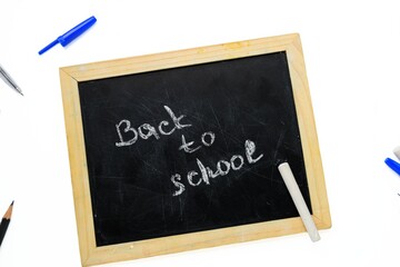 Fototapeta premium A black school board with chalk inscription back to school with pens and pencils on a white background.