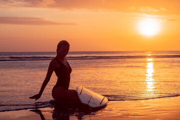 Portrait of surfer girl with beautiful body on the beach with surfboard at colourful sunset time