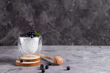 Chia pudding with mint and blueberries in glasses on a wooden stand with a honey stick on a dark background