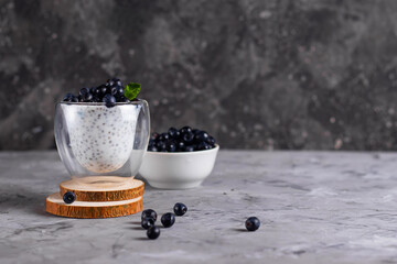 Fototapeta na wymiar Chia pudding with mint and blueberries in glasses on a wooden stand with a plate of blueberries on a light background