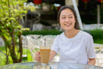 Happy young beautiful Asian woman thinking at the coffee shop outdoors
