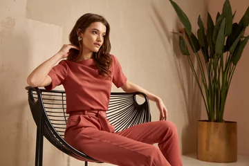 Foto op Plexiglas Beautiful brunette woman natural makeup wear fashion clothes casual dress code office style total pink blouse and pants suit, romantic date business meeting armchair interior stairs flowerpot. © indiraswork