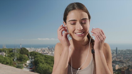 Woman putting on earphones in city of Barcelona. Girl listening music in earbuds